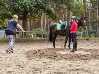 Reiterin mit Pferd in der Mitte des Reitplatzes, Reittrainerin Kathi Stec gibt Anweisungen.