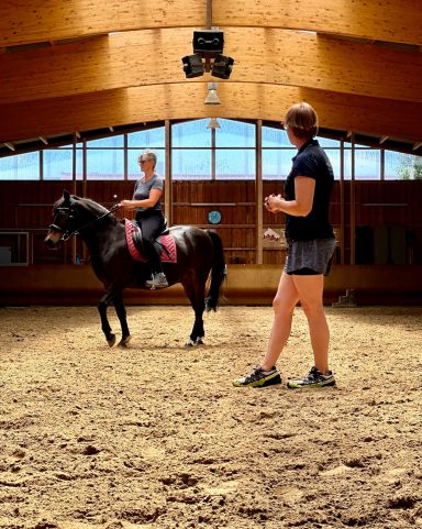 Pferde-Reiterpaar beim Pferde- und Reittraining in einer Reithalle, Trainerin Kathi Stec beobacht.